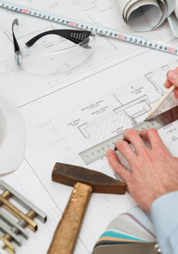 Image of engineer or architectural project, Close up of engineer's hand drawing plan on BluePrint with Engineering tools on workplace.