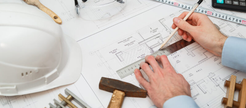 Image of engineer or architectural project, Close up of engineer's hand drawing plan on BluePrint with Engineering tools on workplace.