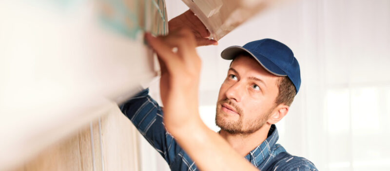 Young workman in workwear looking into system of air conditioner to find out reason of disorder