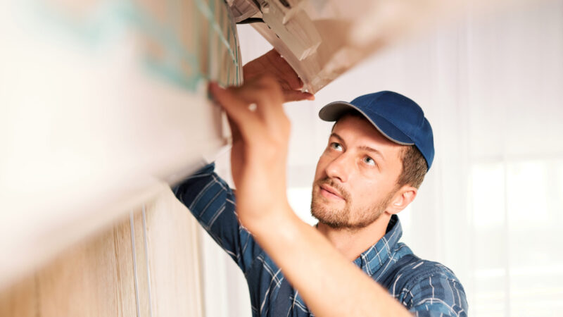 Young workman in workwear looking into system of air conditioner to find out reason of disorder